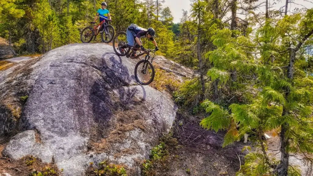 Two mountain bikers on top of a rock enjoying the stunning view while sipping coffee.