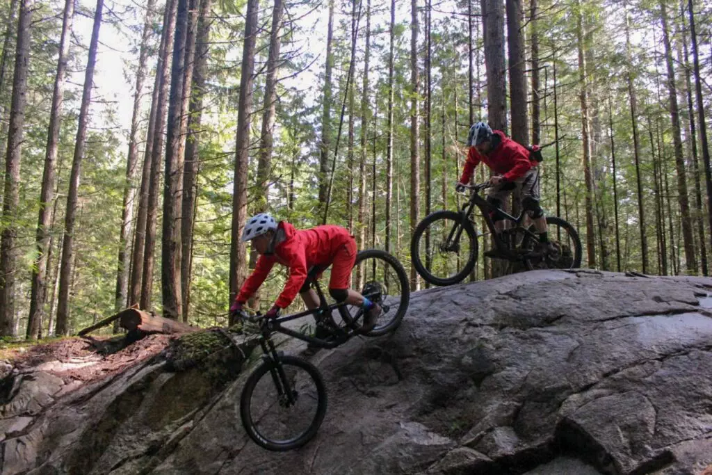 Two adventure-seeking mountain bikers navigating the rugged trails of Squamish, honing their skills through exhilarating mountain bike lessons amid the stunning woodland scenery.