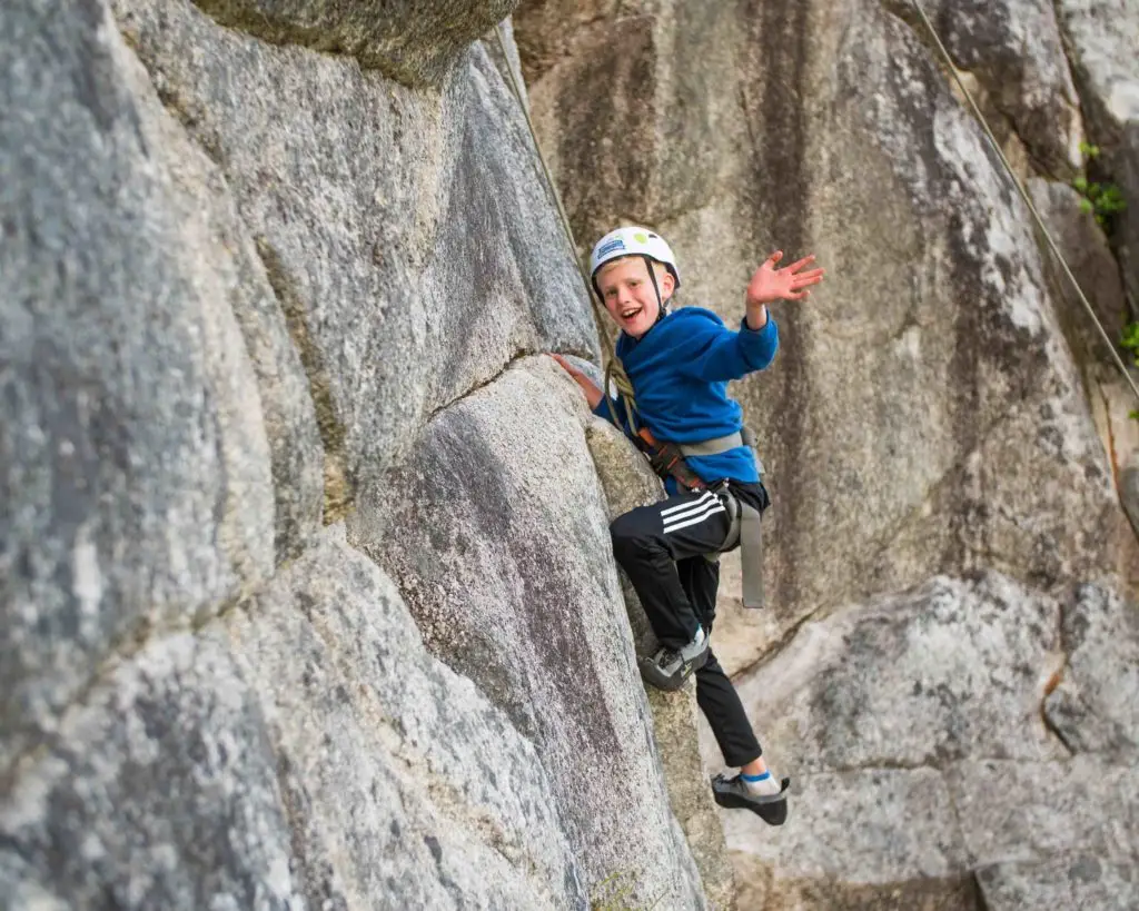 A young boy is climbing up a large rock.