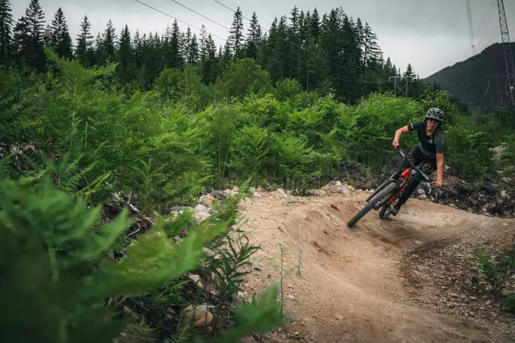 A person wearing a helmet rides a mountain bike on a dirt trail through a forested area.