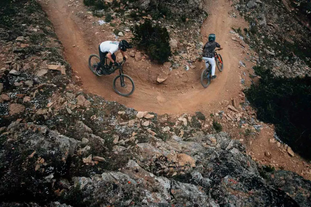 Two cyclists navigate a winding dirt trail on a rocky hillside.