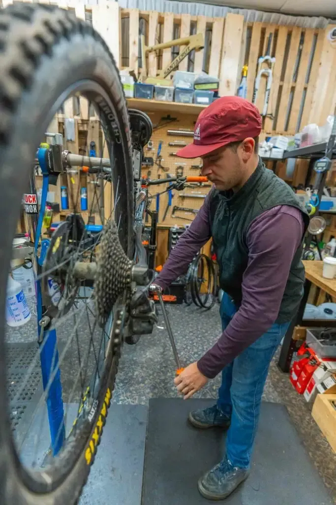 RideHub 15 In a workshop in Squamish, British Columbia, a mechanic wearing a red cap is busy repairing a bicycle, surrounded by essential tools and equipment neatly arranged in the background.